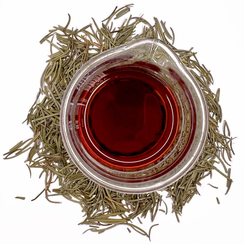 Dried leaves from a Rosemary bush (Rosmarinus officinalis ), which has long stems with small, thin green leaves, surround a beaker of the Native Extracts Rosemary Cellular Extract.